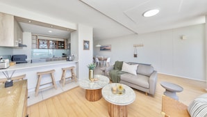 A modern living space with a kitchen area, a dining table, and a sofa. - Dolphin Beach CG12, Blouberg by HMH (Cape Town)