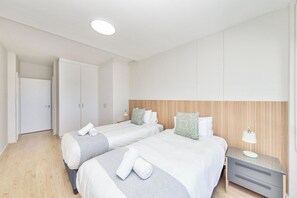 A hotel room with two beds, a wooden headboard, a nightstand with a lamp, and a wardrobe.