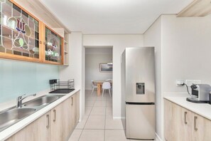Cozinha moderna com eletrodomésticos de aço inoxidável, uma pia dupla e um espaço de jantar com mesa e cadeiras.