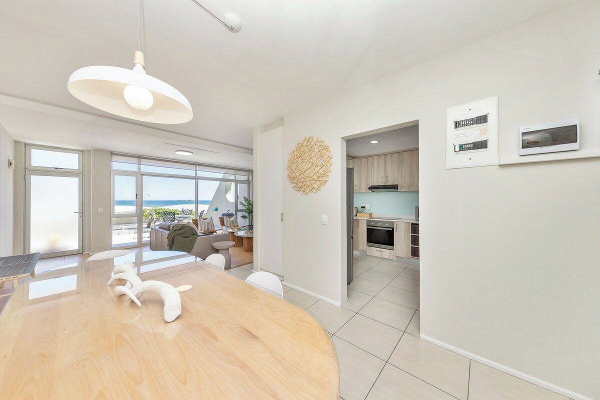 Un interior moderno con una mesa de comedor de madera, una lámpara colgante y vistas a través de un ventanal.