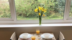 Une table à manger dressée pour quatre personnes, avec des assiettes, des couverts et des verres de jus d’orange.
