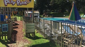 Un espace de jeux pour enfants avec une pancarte indiquant « Parc de jeux de Pirate Pete », une piscine entourée d’une clôture et un petit bâtiment en arrière-plan.