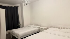 A bedroom with two white beds, a white nightstand, a white dresser, a black curtain, and a chandelier.