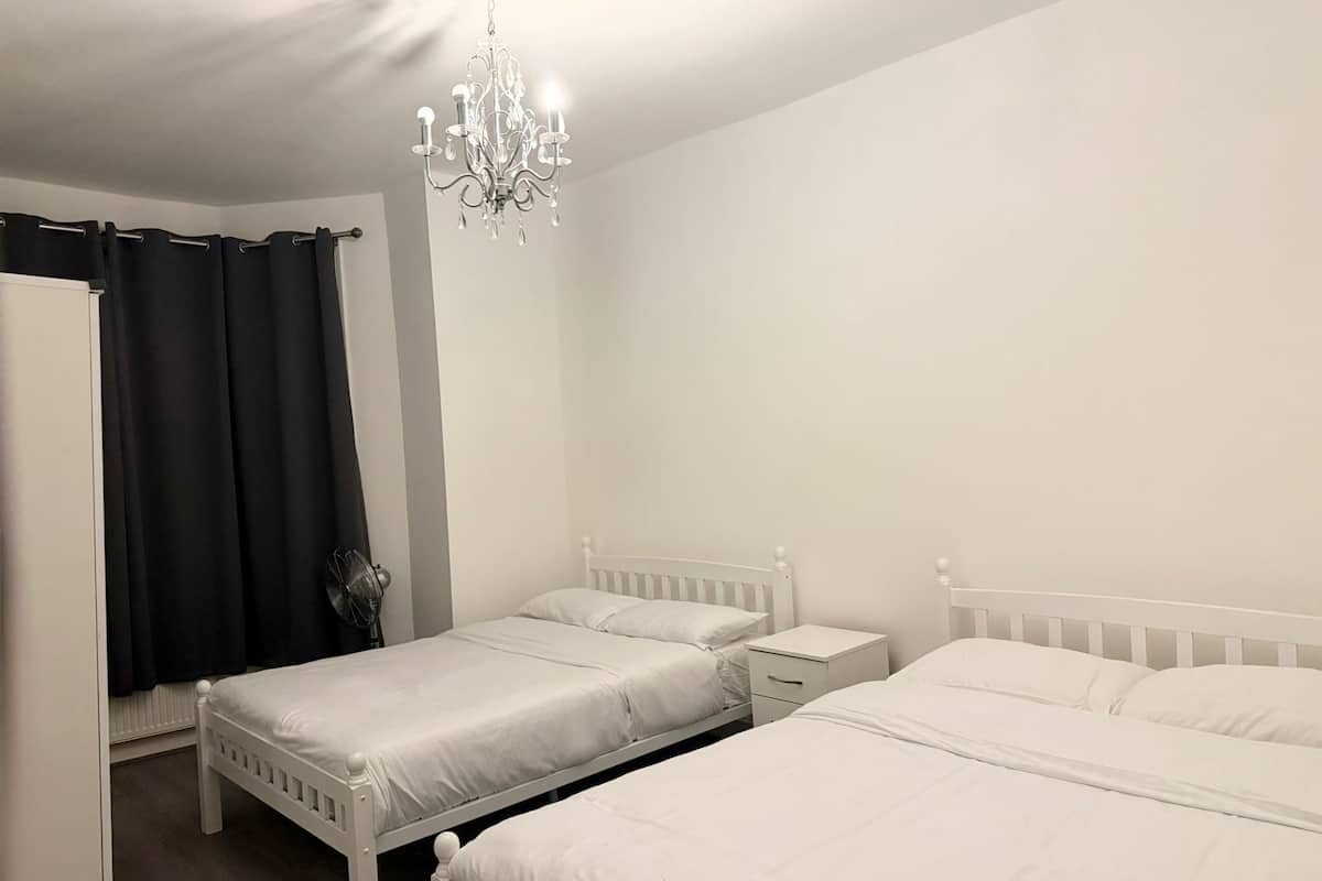 A bedroom with two white beds, a white nightstand, a white dresser, a black curtain, and a chandelier.