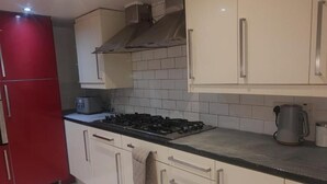 A kitchen with a gas stove, a kettle, and a red refrigerator.