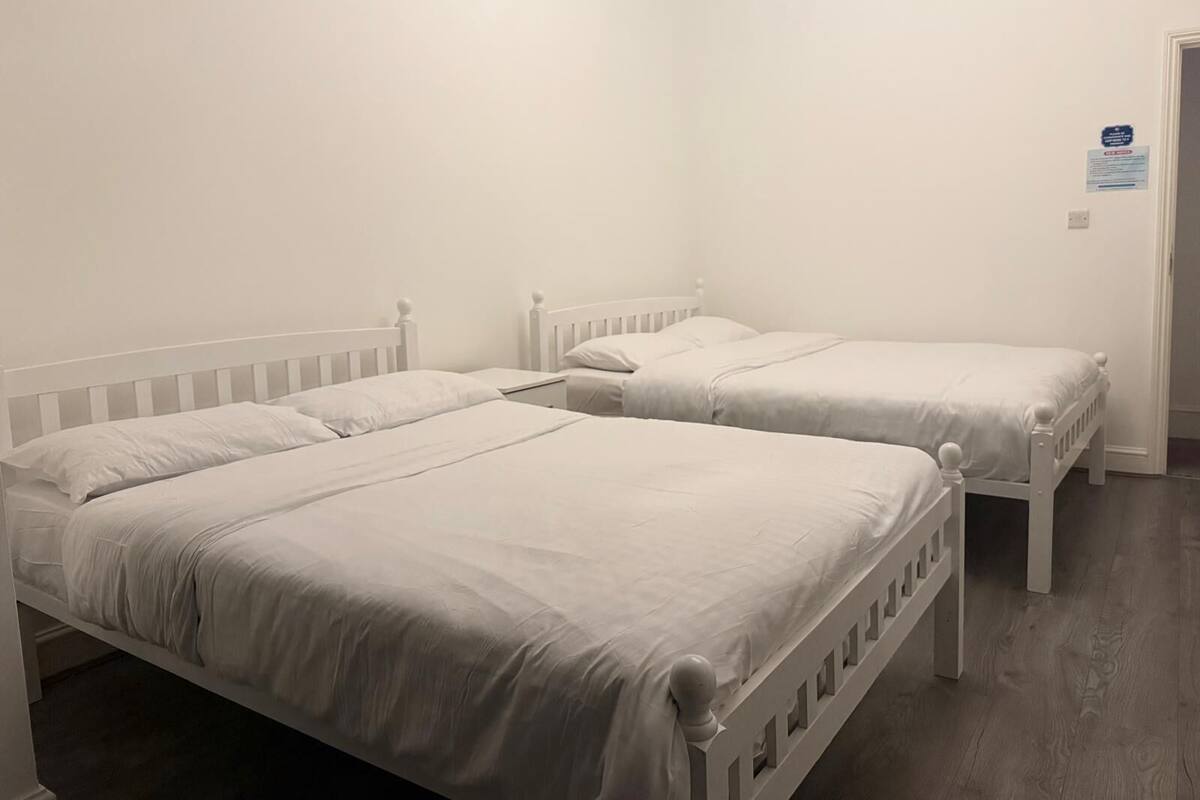 A room with two white beds, a wooden floor, and a white wall.