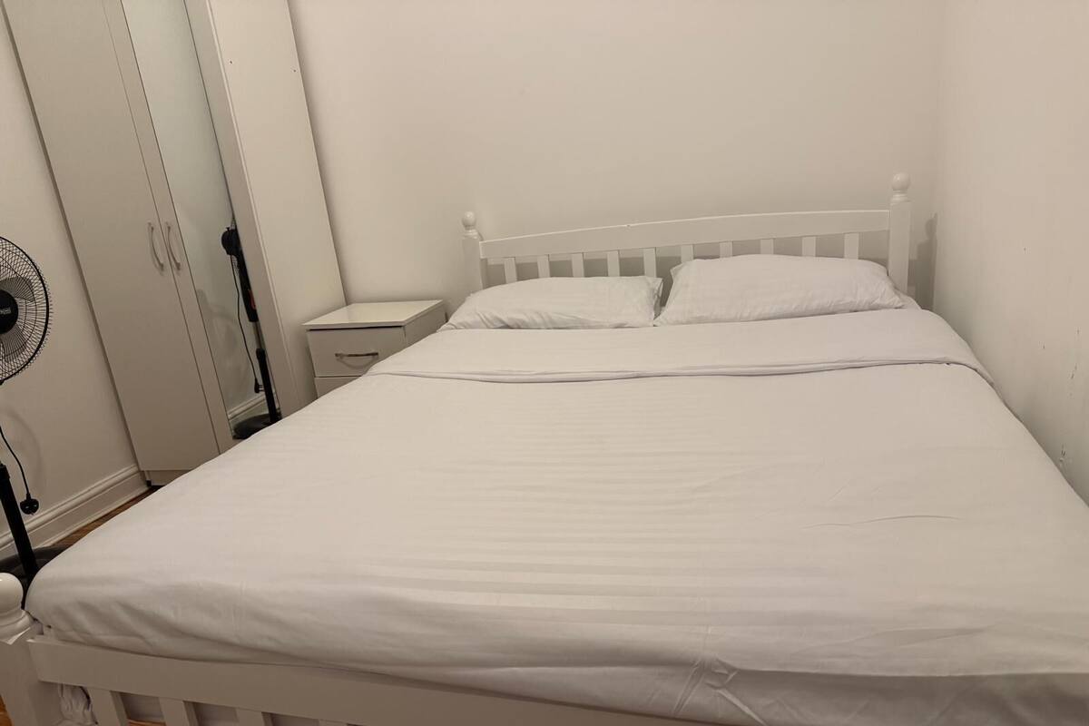 A white bed with a wooden frame, a white nightstand, and a white wardrobe with a mirror.