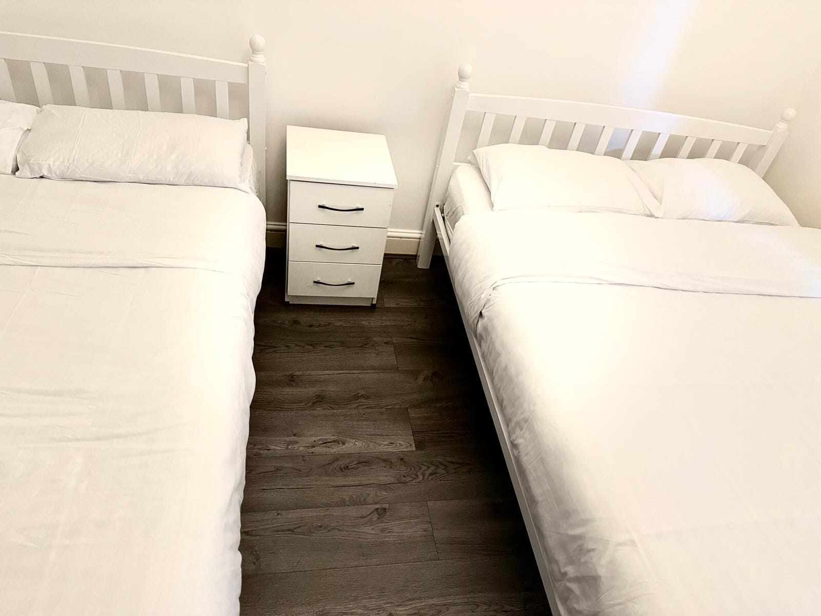 A bedroom with two single beds, a nightstand with drawers, and a wooden floor.