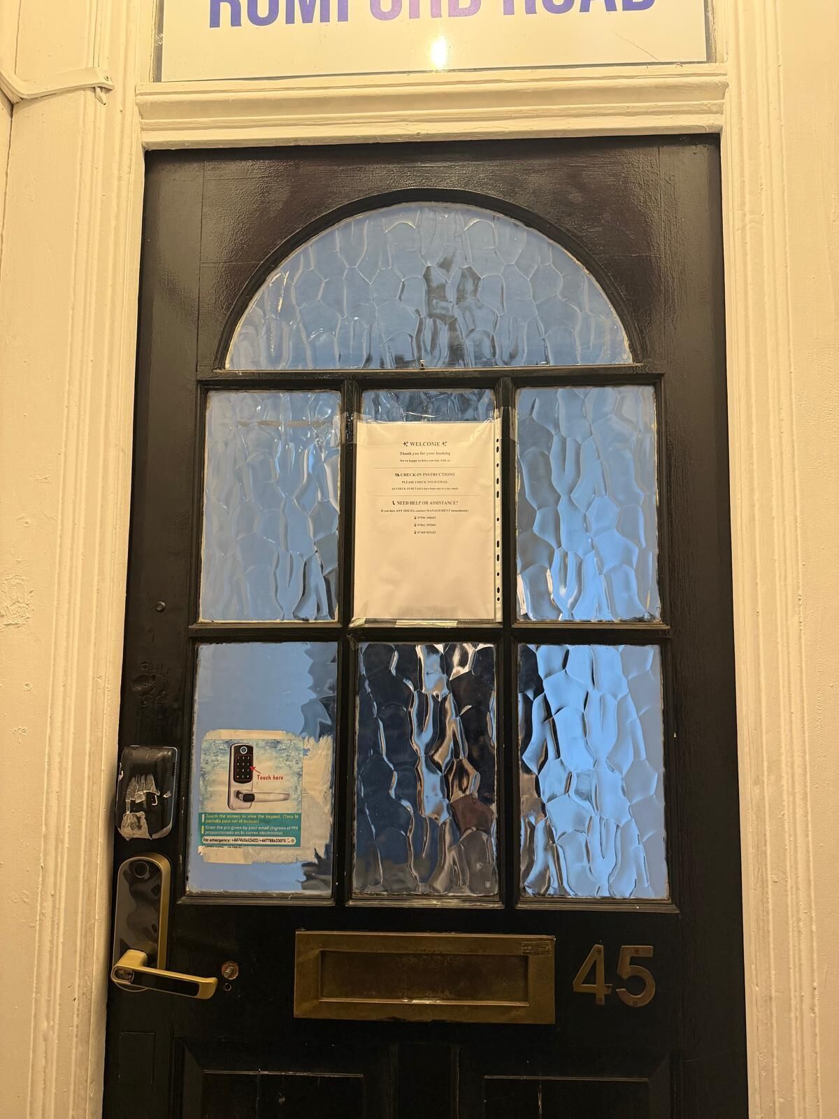 A black door with a glass panel, a brass doorbell, and a handwritten note.