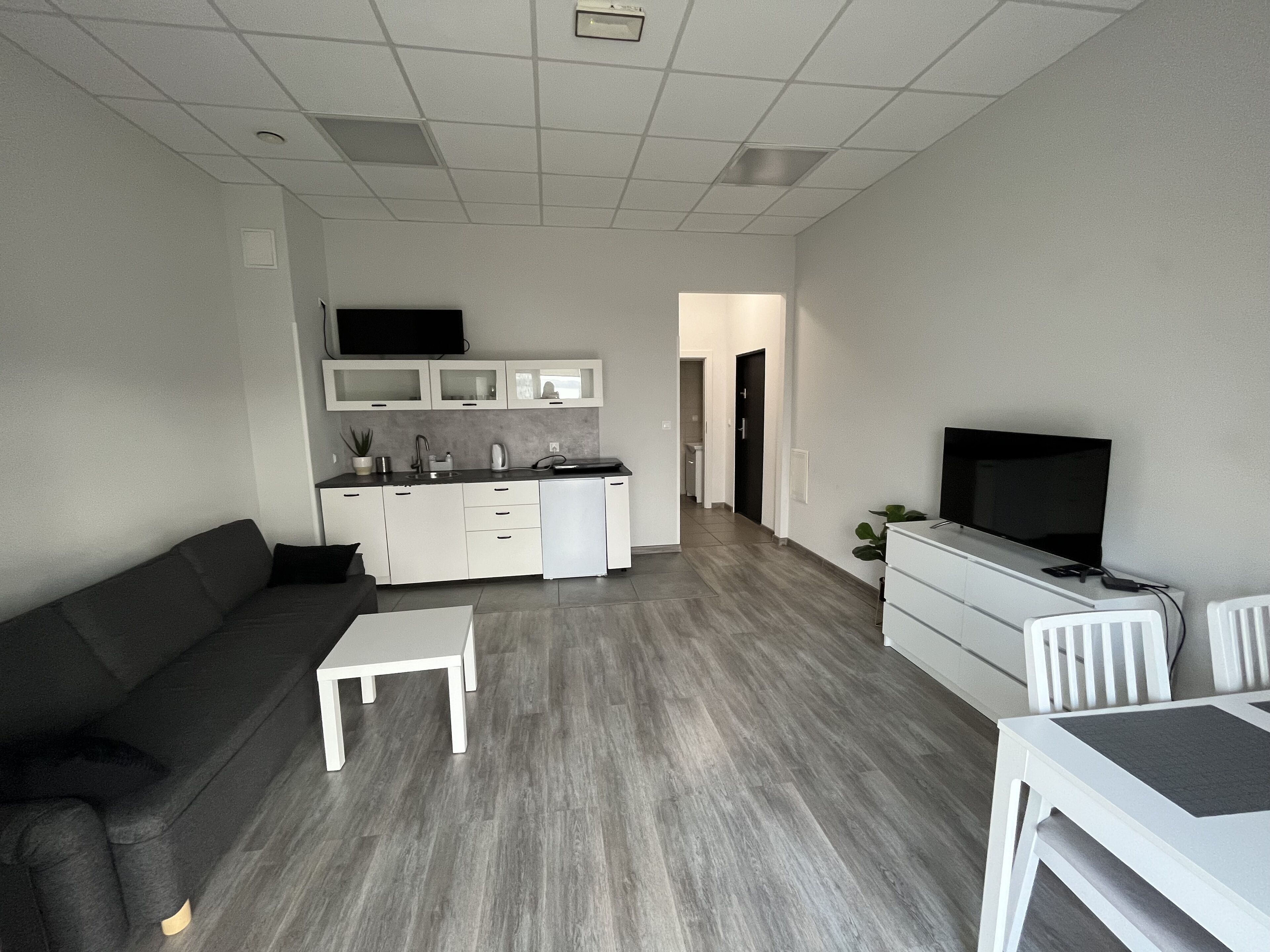 A modern living room with a grey sofa, a small white table, and a TV on a stand.