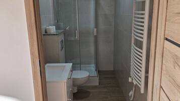 A compact bathroom with a shower, toilet, and a towel rack.