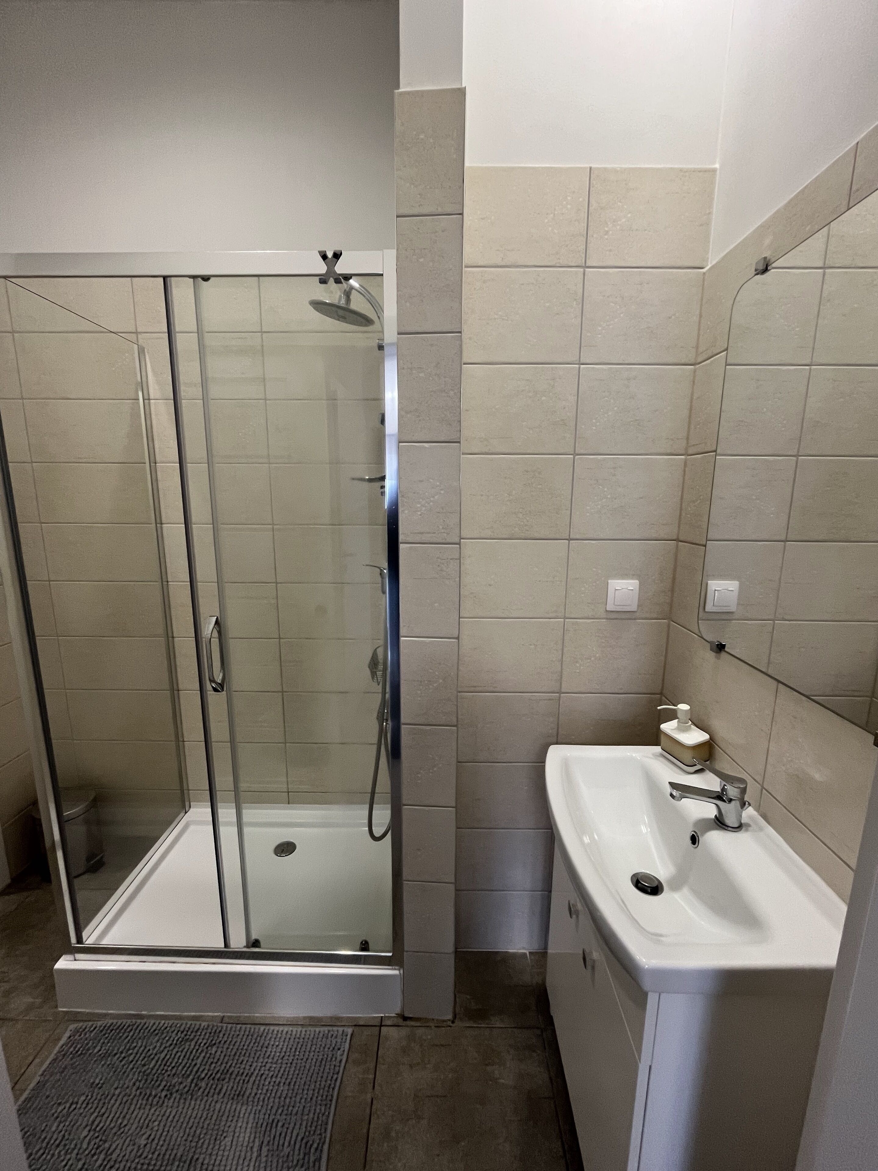 A bathroom with a glass-enclosed shower, a white sink, and beige tiles.