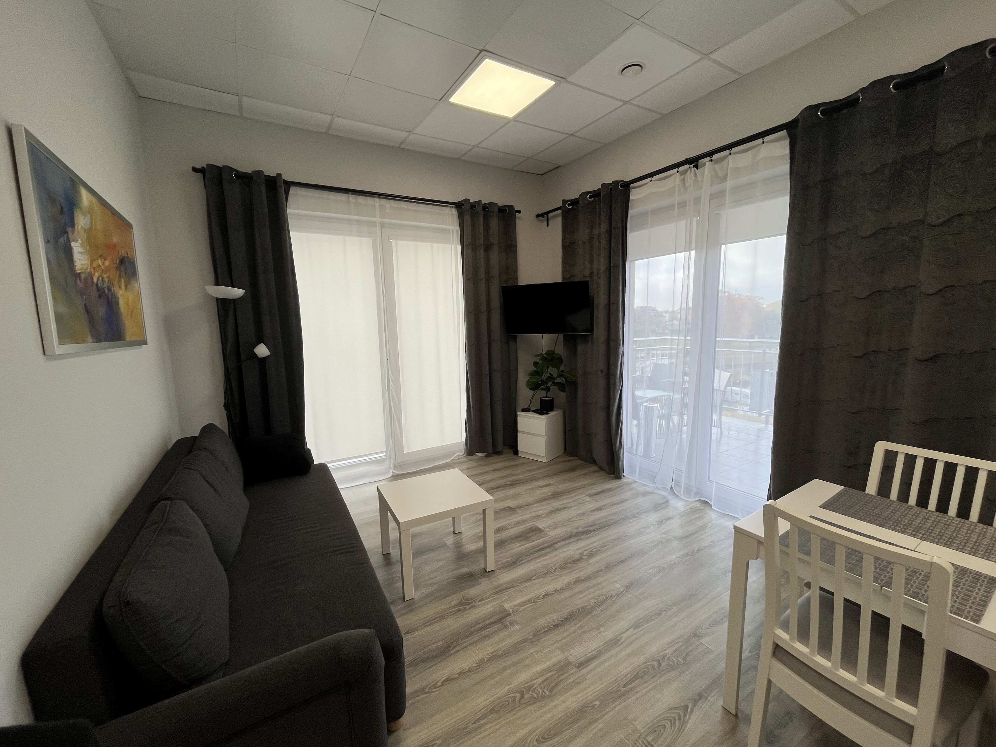A living room with a sofa, a small table, a TV, and a view of the city through large windows.