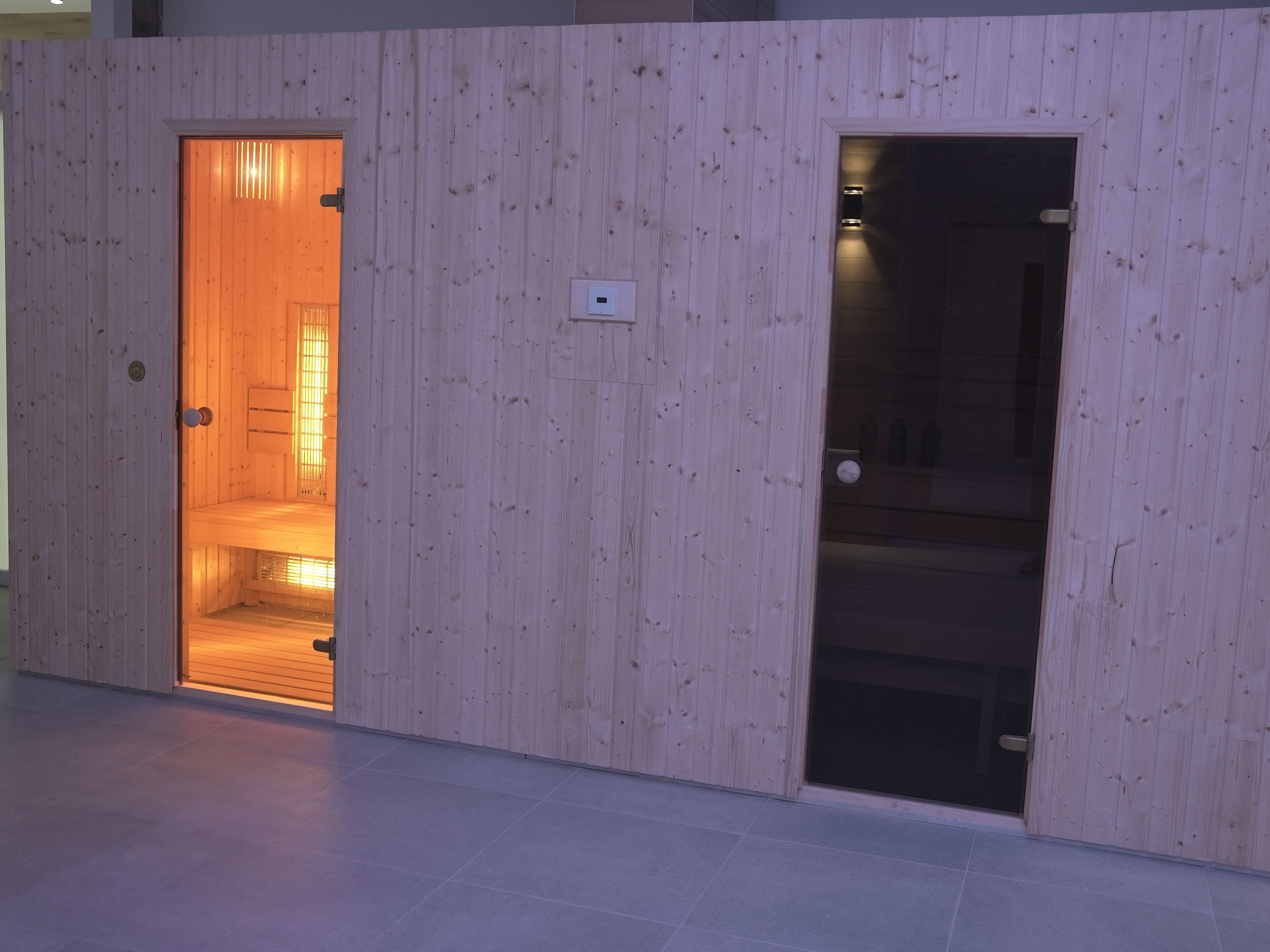 A wooden room with a door leading to a lit interior, a visible light switch, and a tiled floor.