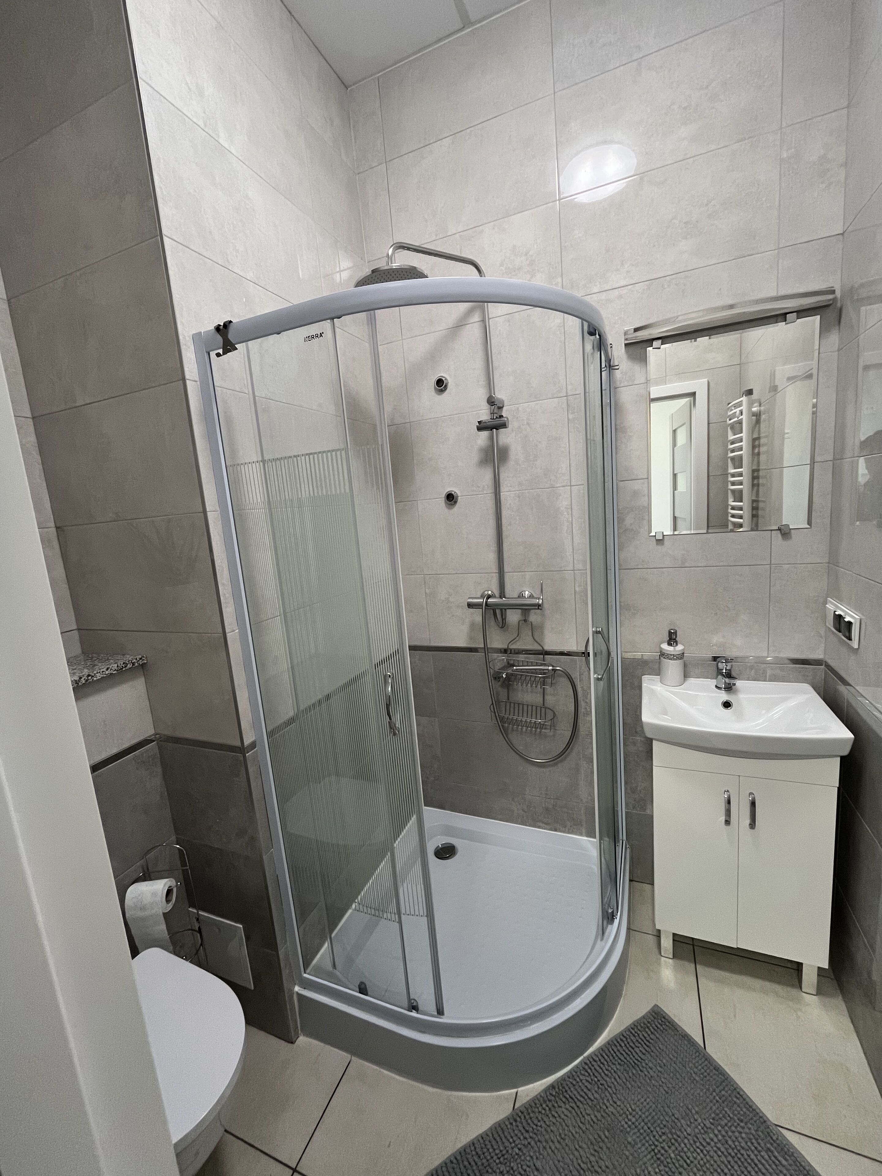 Un baño moderno con ducha envuelta en vidrio, un lavamanos blanco y un espejo sobre él.