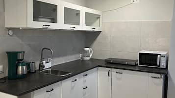 A modern kitchen with white cabinets, a black countertop, a coffee maker, a microwave, and a sink.