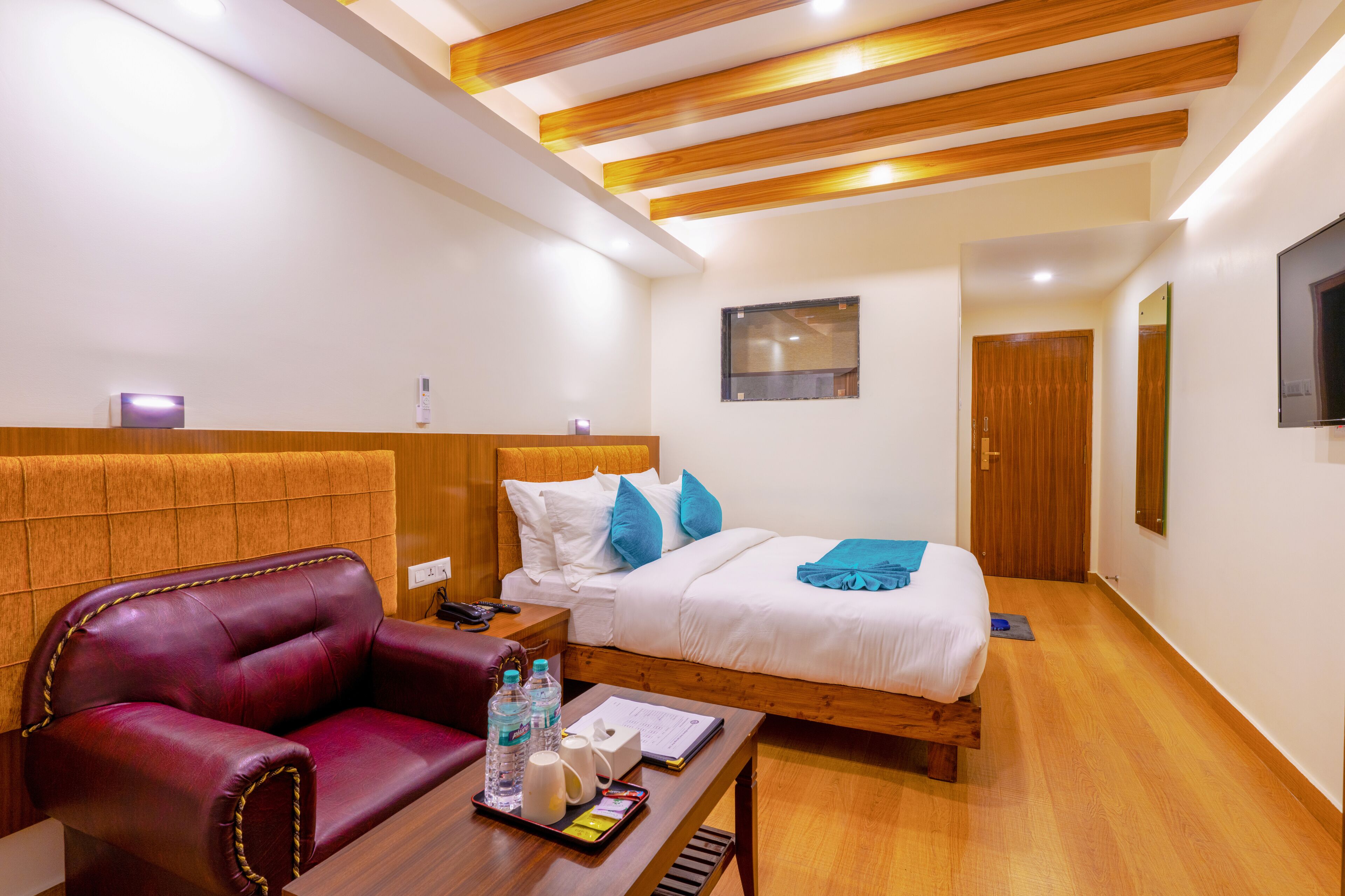 A hotel room with a bed, a red leather chair, a wooden table with toiletries, and a wooden ceiling.