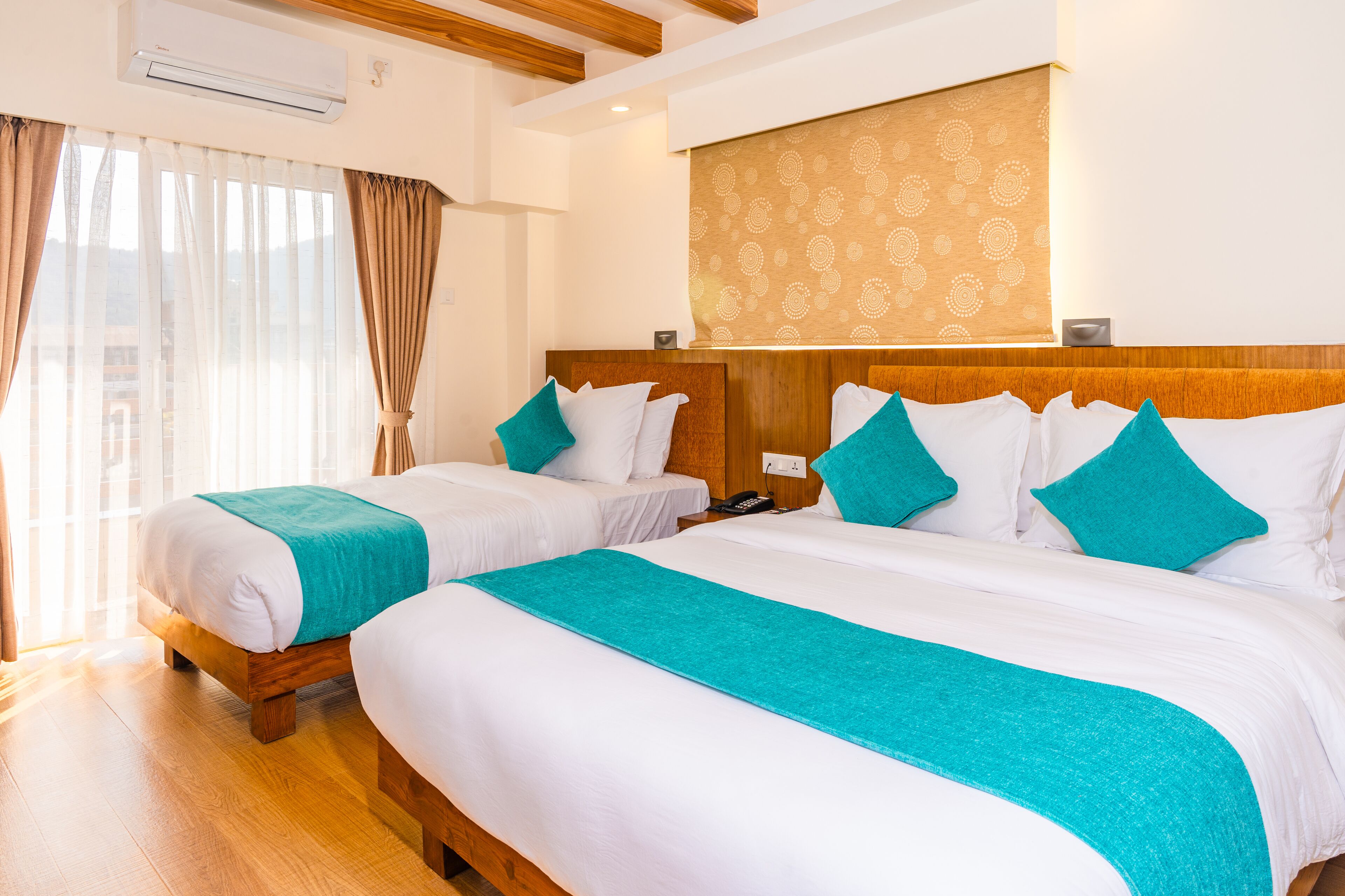 Habitación de hotel con dos camas, cada una con ropa de cama blanca y detalles verde azulado, cabeceros de madera y un tapiz de pared estampado.