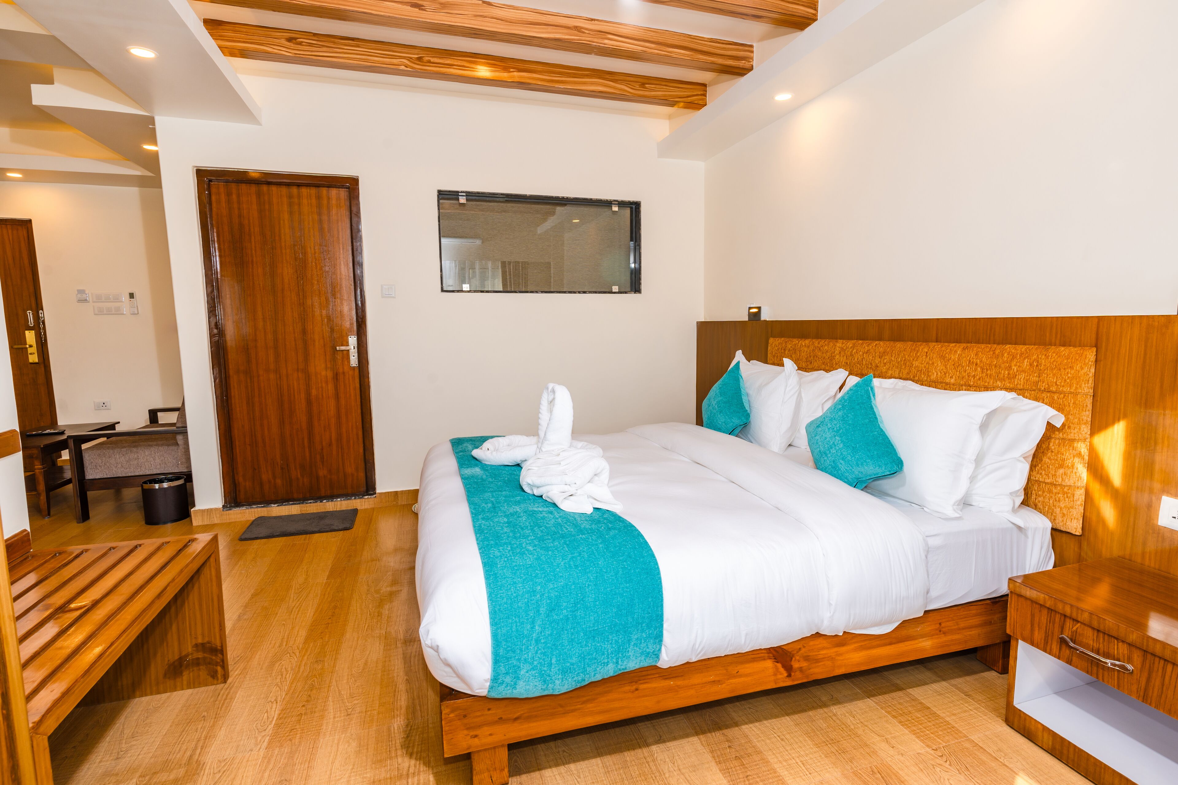 A modern hotel room with a wooden bed, a wooden bench, a small table, and a wooden nightstand.