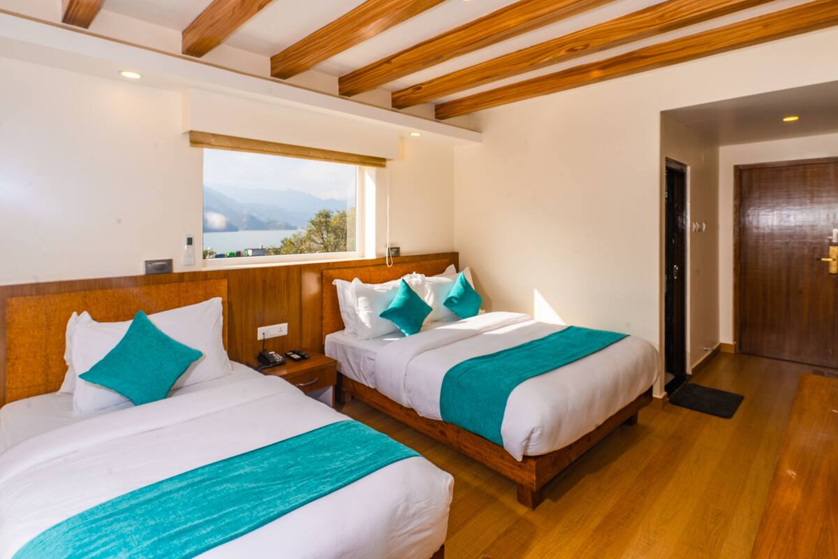 A hotel room with two beds, wooden headboards, a window with a view, and a wooden door.