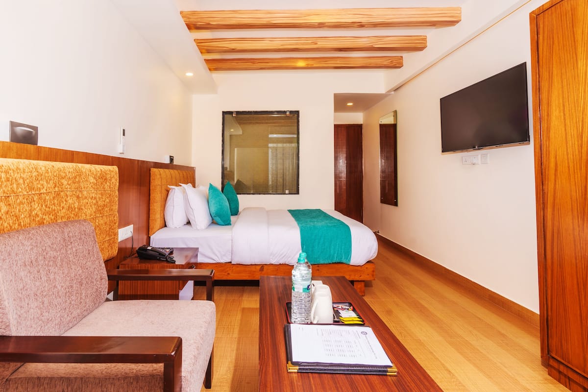 A hotel room with a bed, a sofa, a wooden ceiling, a TV, and a wooden wardrobe.