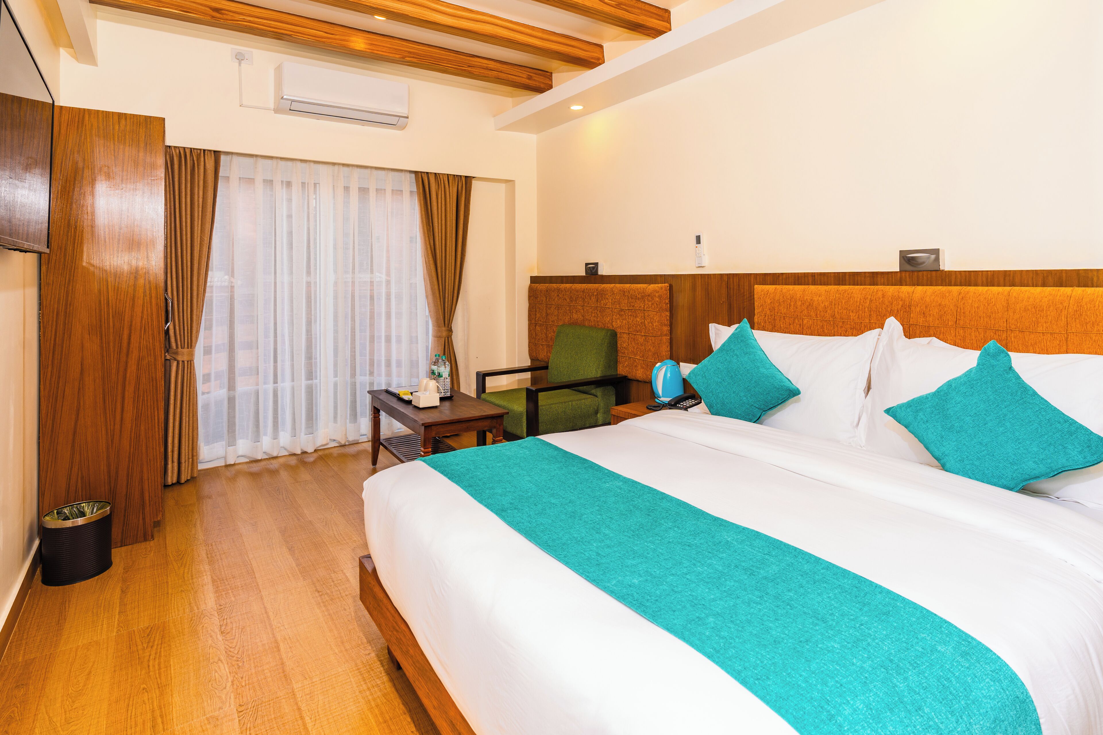 A hotel room with a large bed, a wooden headboard, a desk with a chair, and a window with curtains.
