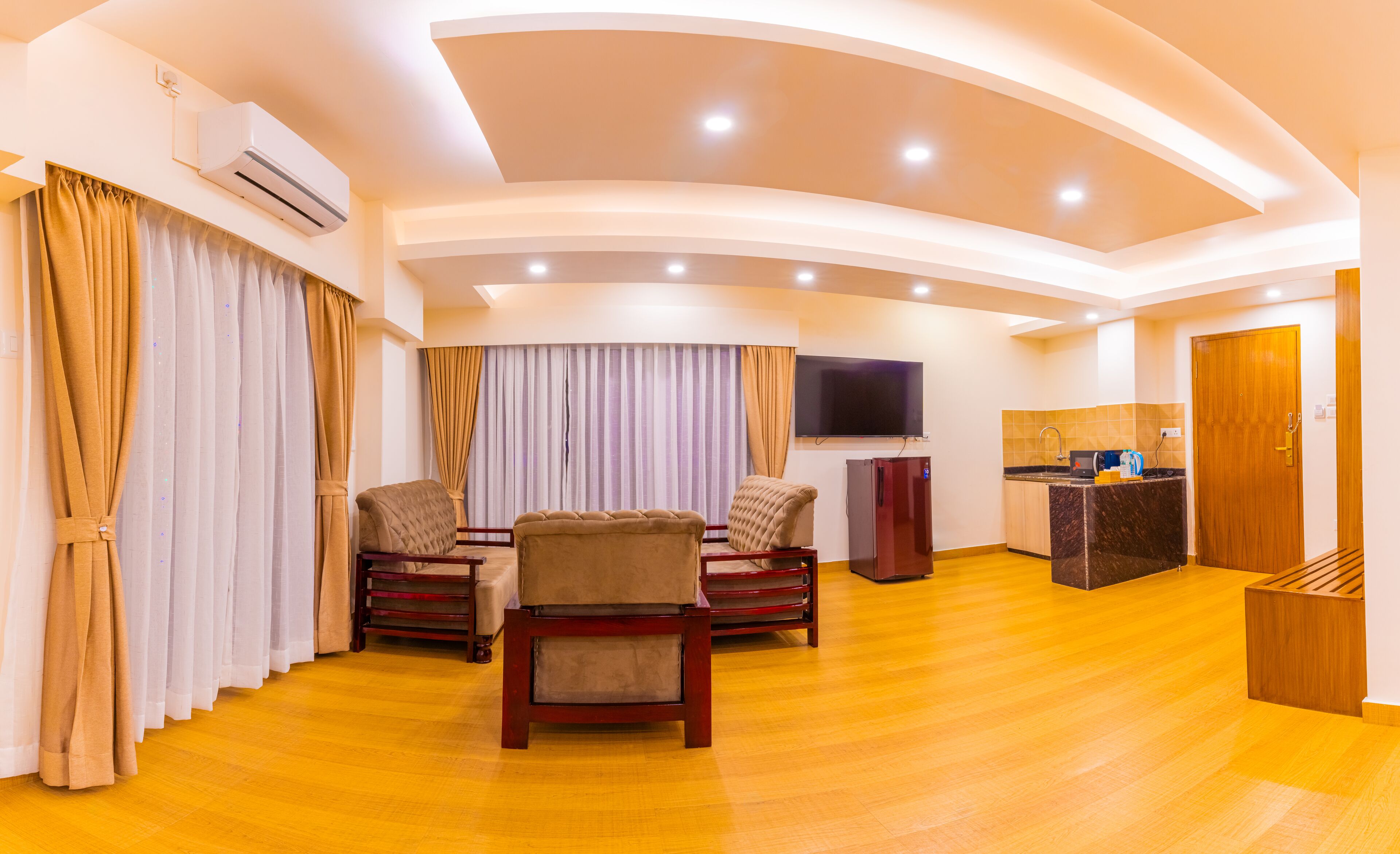 Amplia sala de estar con mesa de comedor, sillas, televisor de pantalla plana, zona de cocina y puerta de madera.