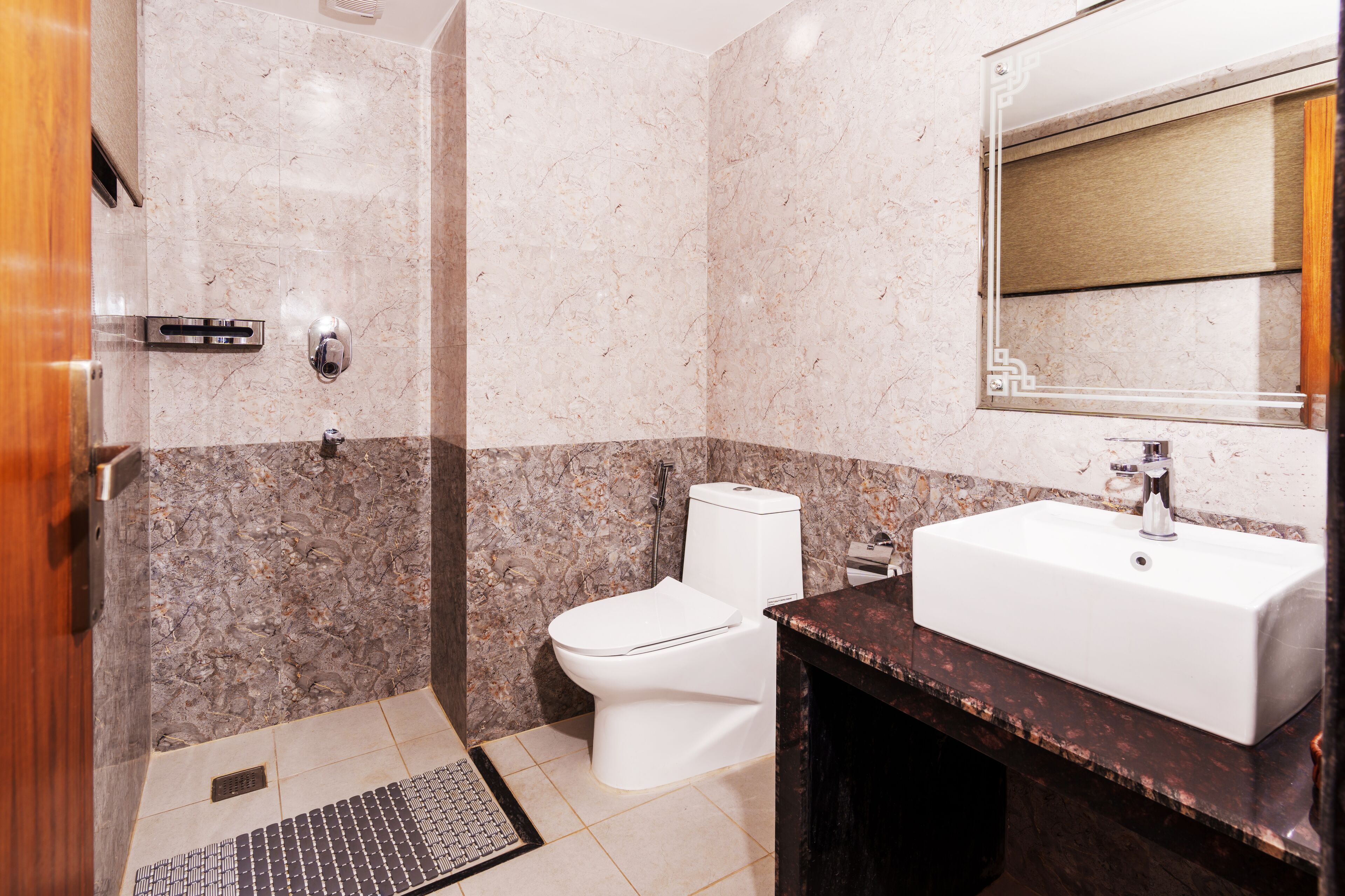 Une salle de bain avec un mur en marbre, des toilettes blanches, un lavabo avec un miroir et un espace douche.