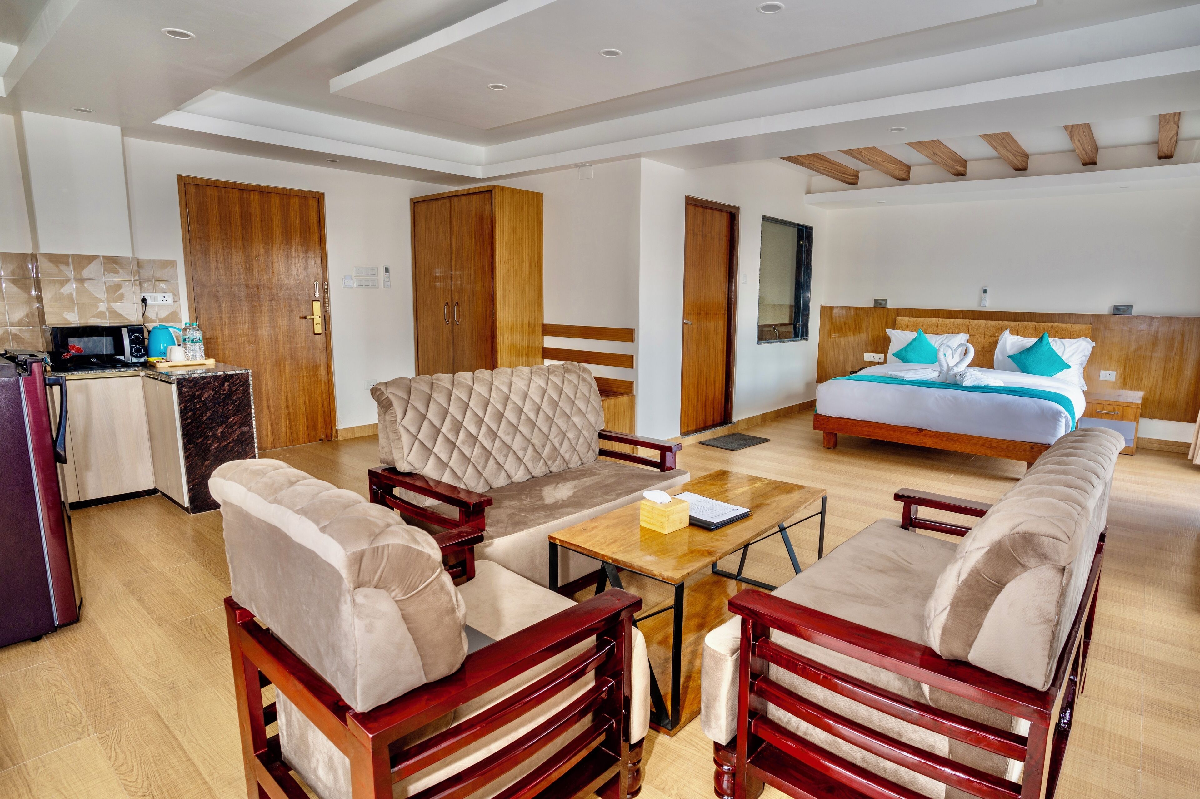 A modern hotel room with a bed, sofa, dining table, and a kitchenette.