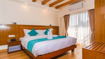 A hotel room with a wooden bed, a nightstand, a desk, and a large window with curtains.