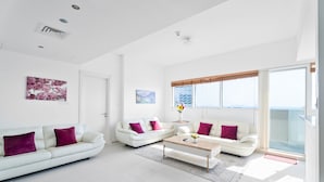 Ein geräumiges Wohnzimmer mit weißen Sofas und einem Couchtisch, großen Fenstern mit Blick und einem modernen Deckenbau.