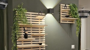 Un espacio de oficina moderno con una pared de acento verde oscuro, estantes de listones de madera y plantas en macetas.
