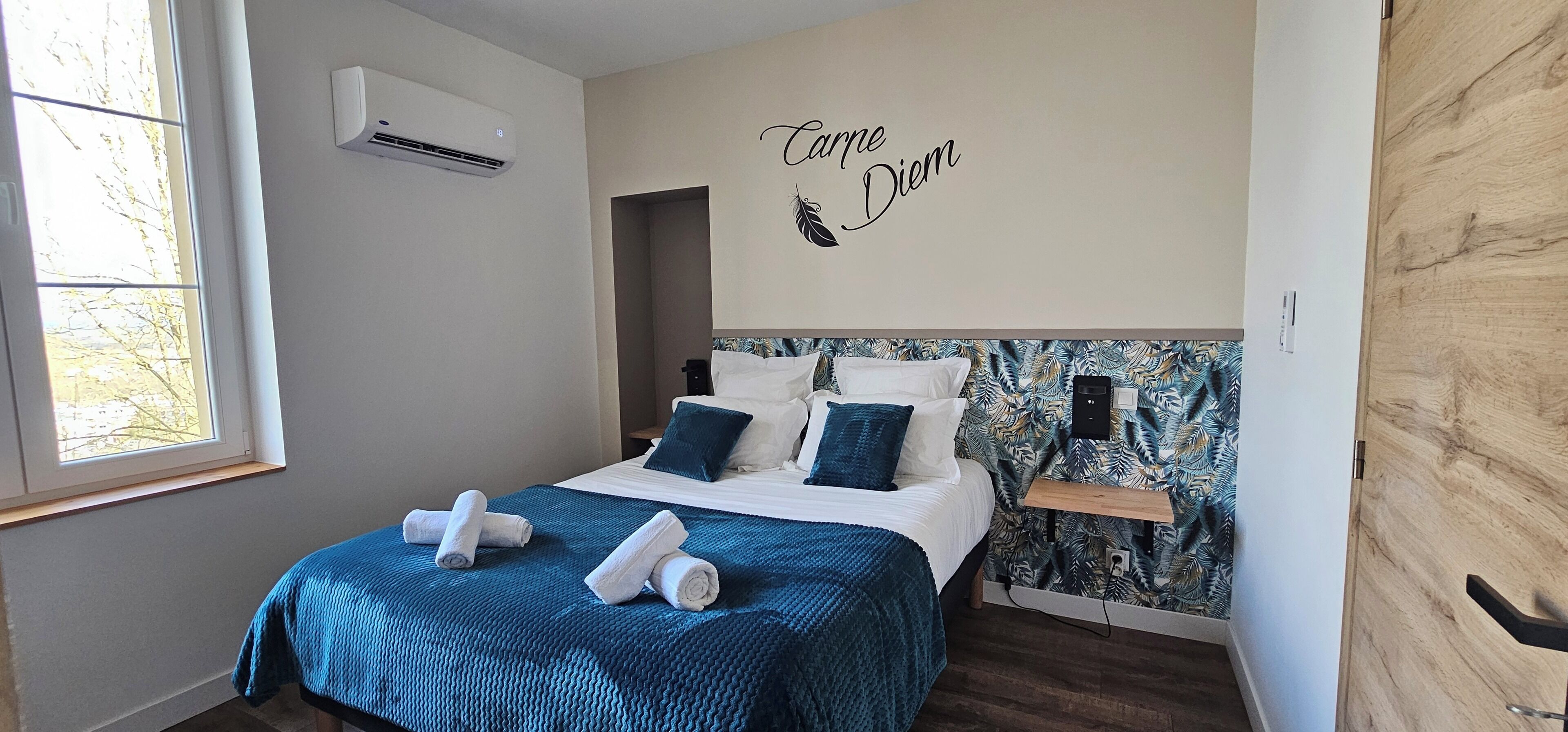 A bedroom with a bed, a wall-mounted air conditioner, a window, and a wall decal with text and a feather design.