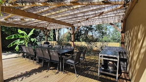 Un patio techado al aire libre con cubierta de madera, una mesa larga con sillas y una zona de barbacoa.