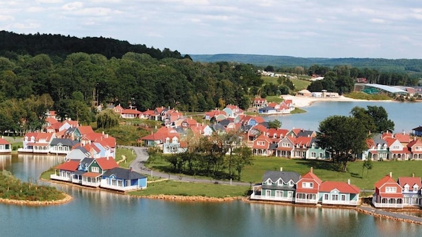 Zona residencial a orillas del lago, con casas de techos rojos y paredes blancas, rodeada de vegetación y un lago.