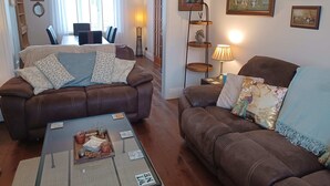 Una sala de estar con dos sofás marrones, una mesa de centro de vidrio y una zona de comedor con una mesa y sillas.