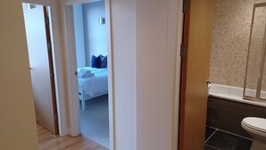 Een hotelkamer met een houten vloer, een bed met wit beddengoed, en een badkamer met een bad en een toilet.