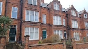 A row of red brick terraced houses with white-framed windows and green doors.