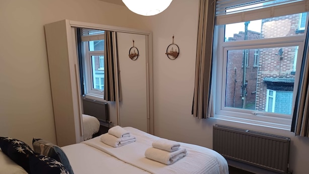 Et hotelværelse med en seng, et stort spejl, et vindue med gardiner og en radiator.