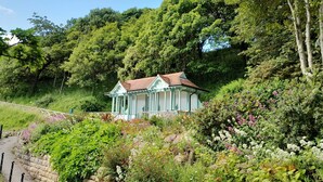 A small, light blue building with a red roof, surrounded by lush greenery and flowering plants. - Edie's Hideaway Summa (Scarborough)