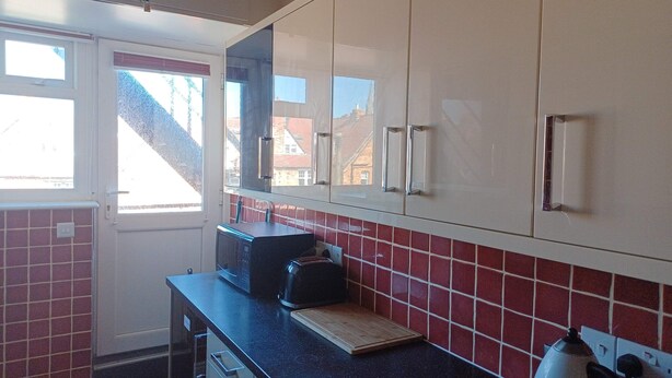 A kitchen with white cabinets, a black countertop, a microwave, and a kettle. - 25 Avenue Victoria, Flat 2 (Scarborough)