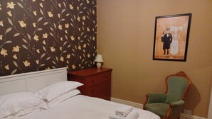 A neatly made bed with white linens and towels, a wooden nightstand with a lamp, a green upholstered chair, and a framed poster on the wall. - 25 Avenue Victoria, Flat 2 (Scarborough)