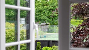 En tennisbane med net, omgivet af frodigt grønt og træer.