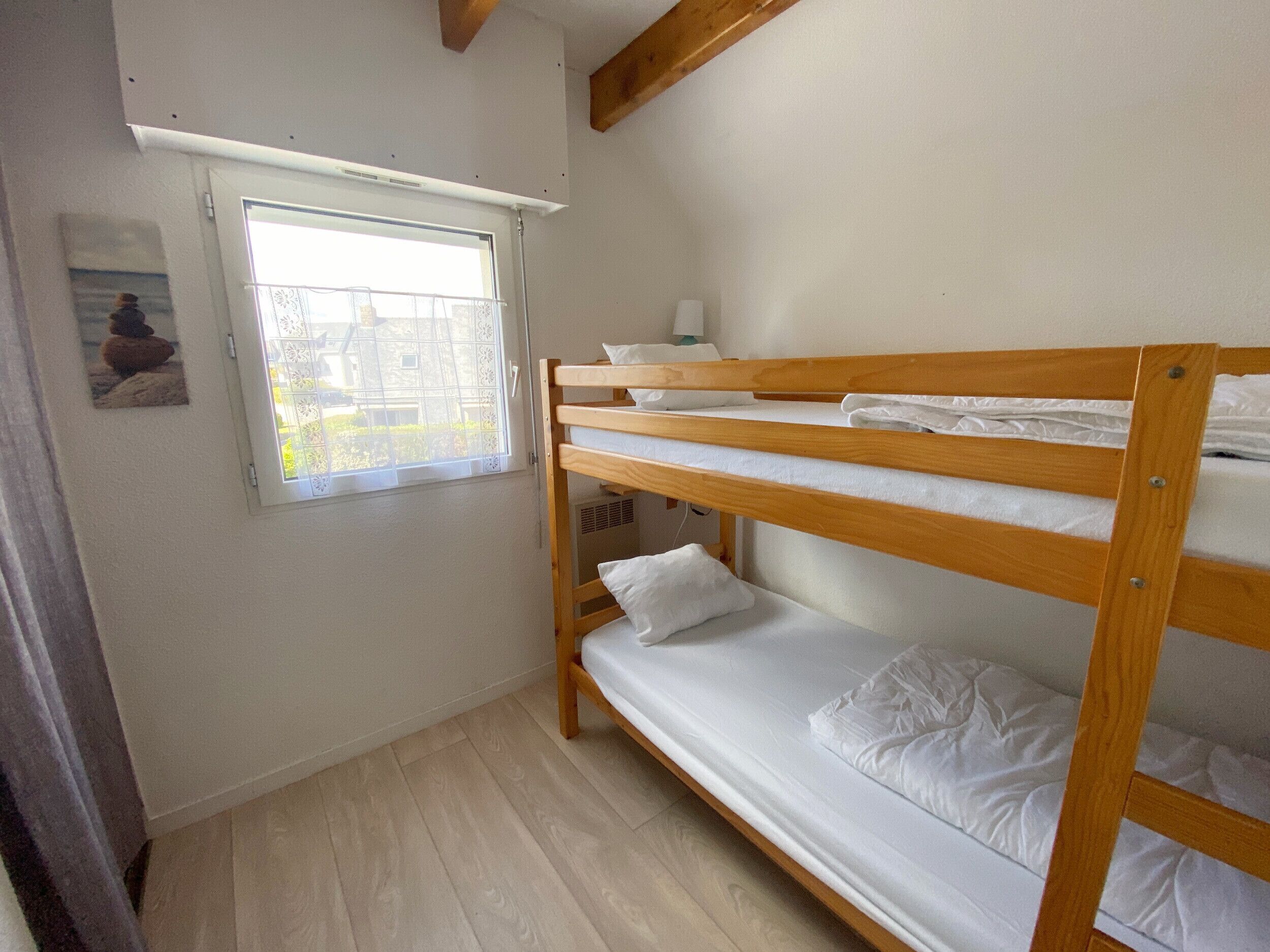 Quarto com beliche, janela, vigas de madeira e um quadro na parede.