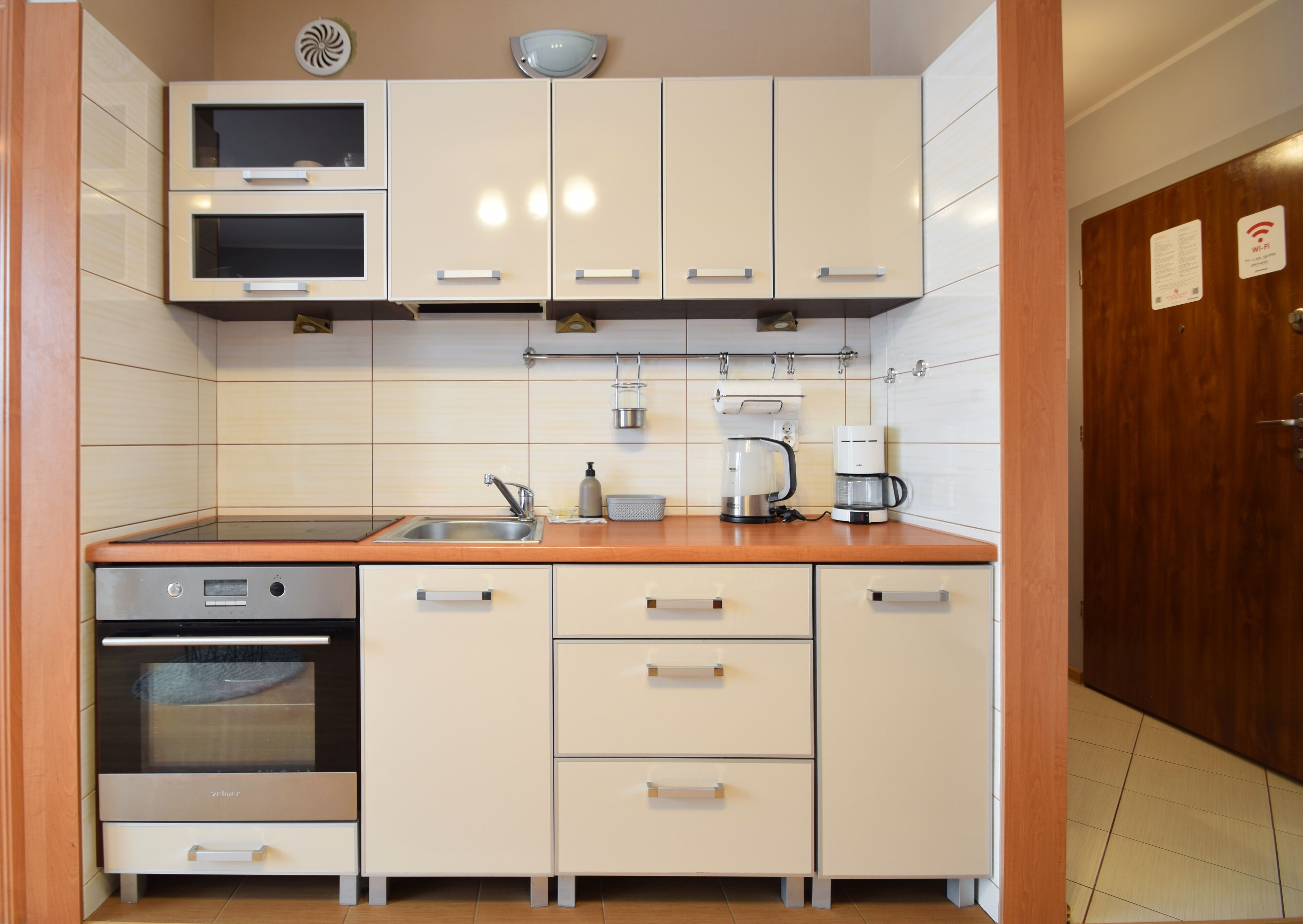 A compact kitchen with white cabinets, a built-in oven, a sink, and a coffee maker.