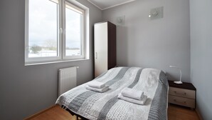 A bedroom with a bed, a nightstand, a dresser, a window, and a radiator. - RentPlanet - Apartament Bałtycka (Kolobrzeg)