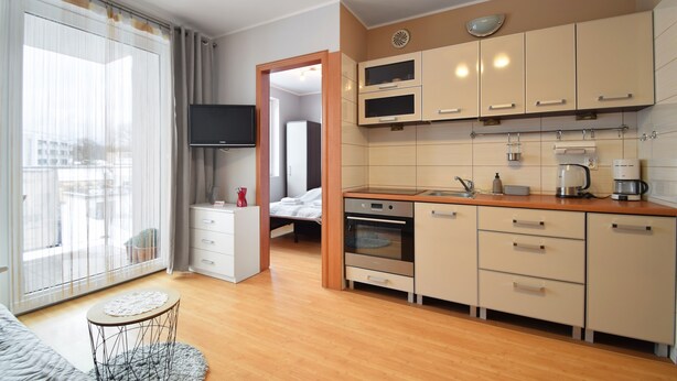 A modern kitchen with a flat-screen TV, a coffee machine, and a dining area with a small round table. - RentPlanet - Apartament Bałtycka (Kolobrzeg)