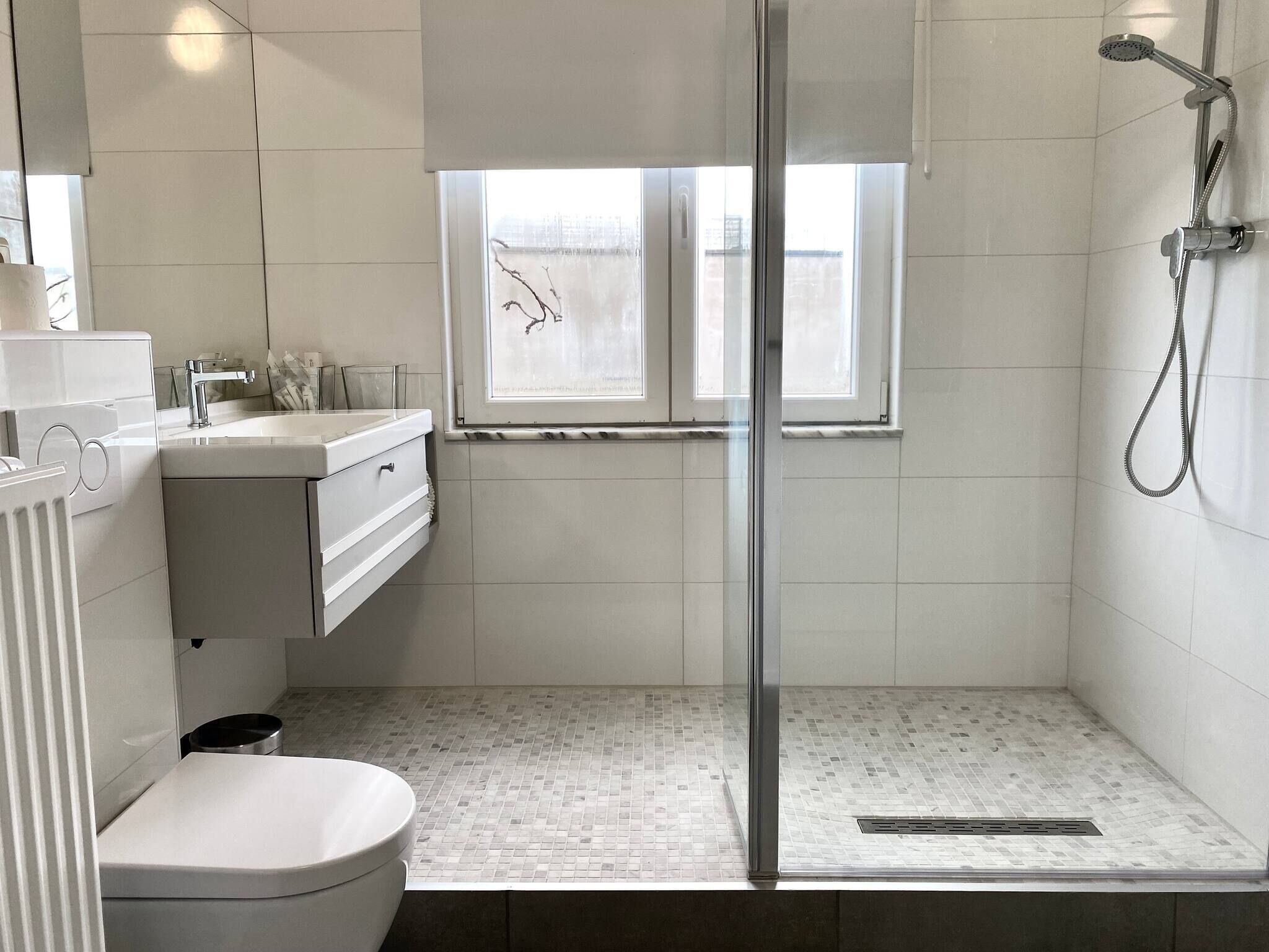 A modern bathroom with a glass shower enclosure, a toilet, a sink with a mirror, and a window.