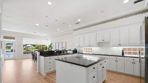 A spacious kitchen with white cabinetry, a large island, and a view through the glass door. - Lakefront House with Huge Swim Spa (Montgomery)