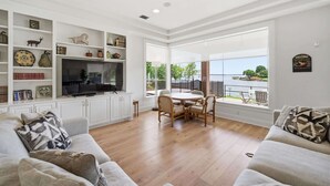 A living room with a TV, white shelves, a dining table, and a view of the outdoors. - Lakefront House with Huge Swim Spa (Montgomery)